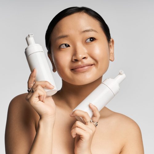 cheerful-young-asian-woman-displays-skincare-produ-min cheerful-young-asian-woman-displays-skincare-produ-min